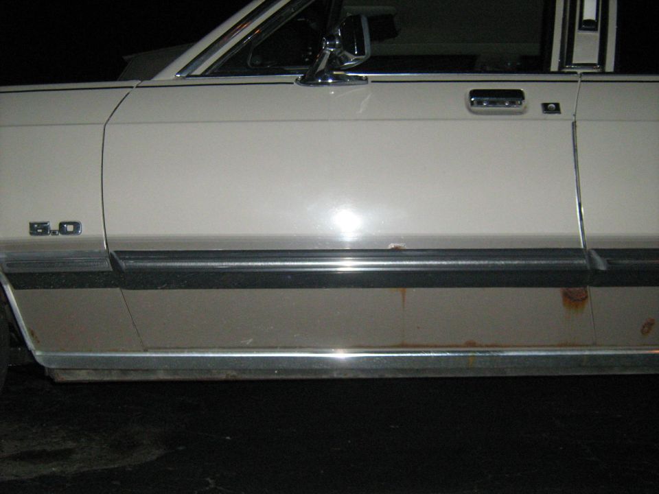 Side view of a beige car with a '5.0' badge and rust on the lower body trim