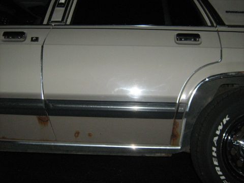 1988 Mercury Grand Marquis - The side of a white 1988 Mercury Grand Marquis shows rust damage on the lower body panels and chrome trim.