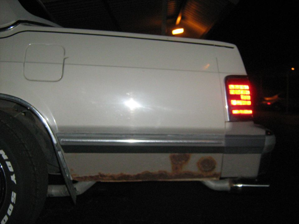 1988 Mercury Grand Marquis rear quarter panel with rust on the lower body and a rectangular taillight