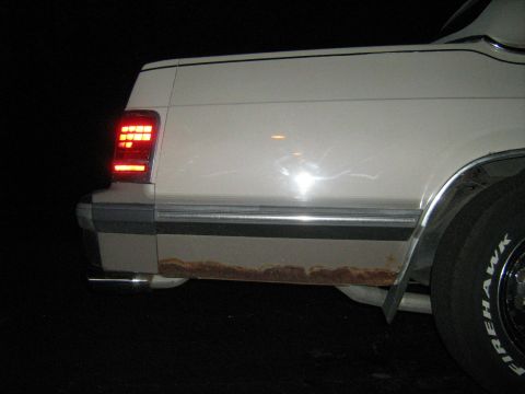 1988 Mercury Grand Marquis - The lower rear body panel of a white vehicle shows significant rust damage.