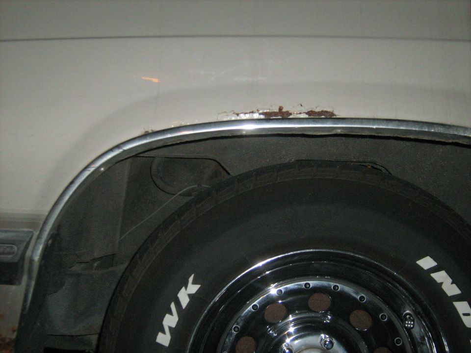 Close-up of rust on the wheel well trim above a tire with chrome wheels