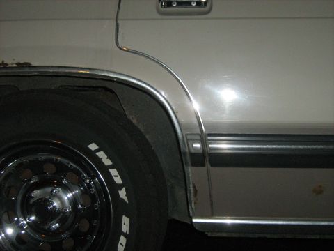 1988 Mercury Grand Marquis - Close-up of a car's side panel and wheel, revealing chrome accents and signs of wear.