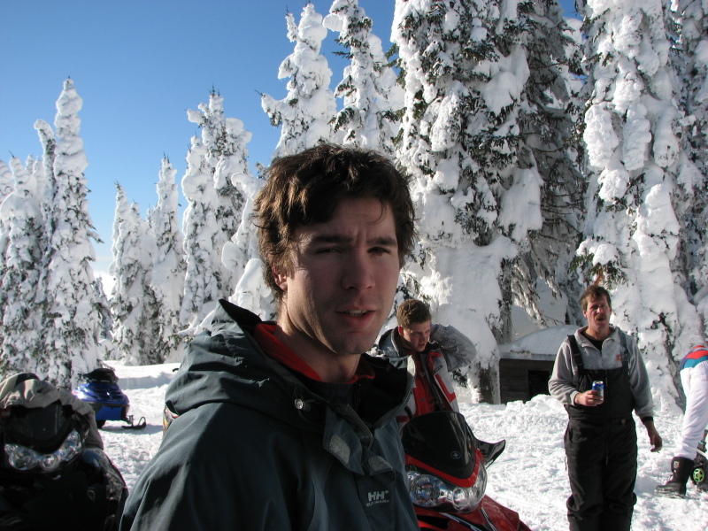 Riders standing among rime-covered trees with red and blue snowmobiles parked behind