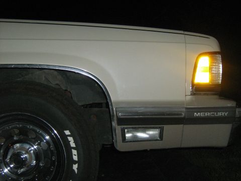 1988 Mercury Grand Marquis - Front corner of a white 1988 Mercury Grand Marquis, showing the turn signal and fender trim.