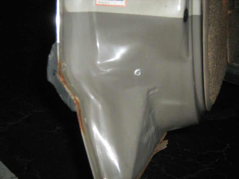 Close-up of a dented gray body panel with rust at the bottom edge