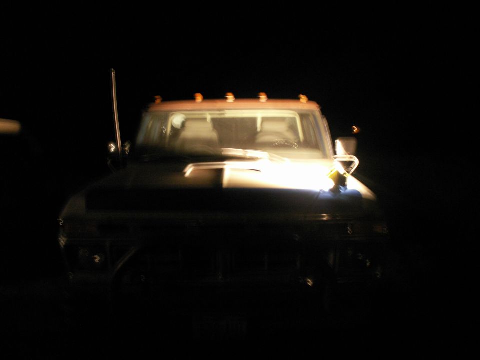 Front view of a dark 1977 Ford F-250 pickup truck at night, illuminated by headlights.