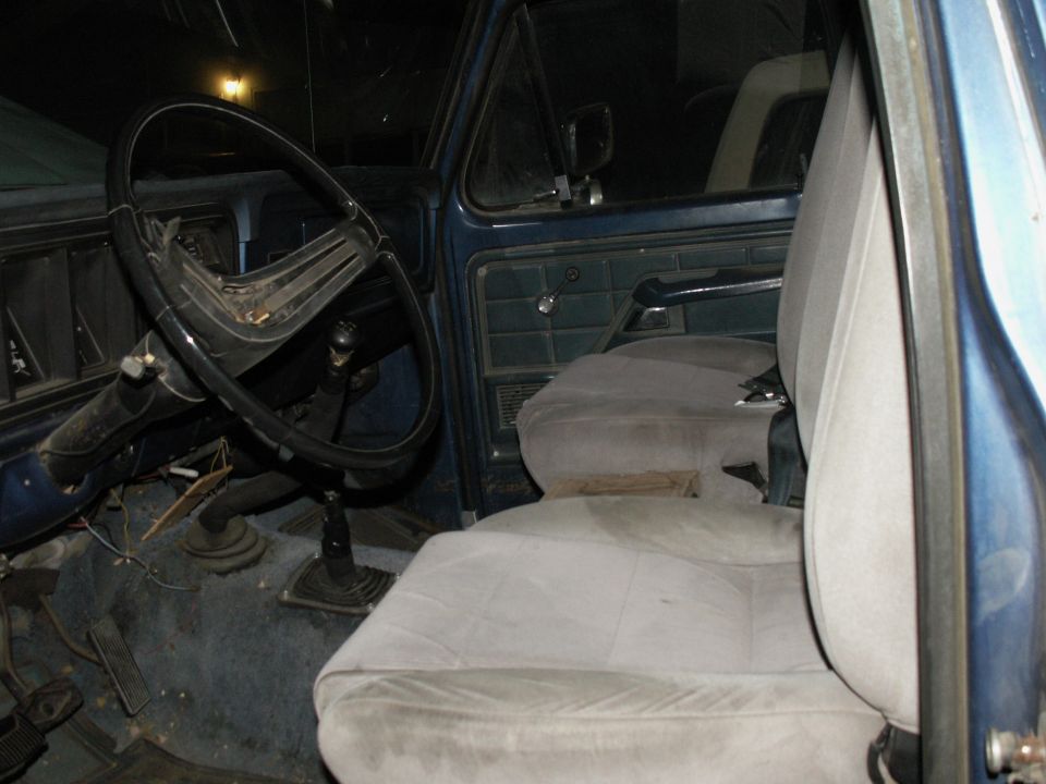 Interior of a blue 1977 Ford F-250 pickup truck showing steering wheel, bench seat, and floor.