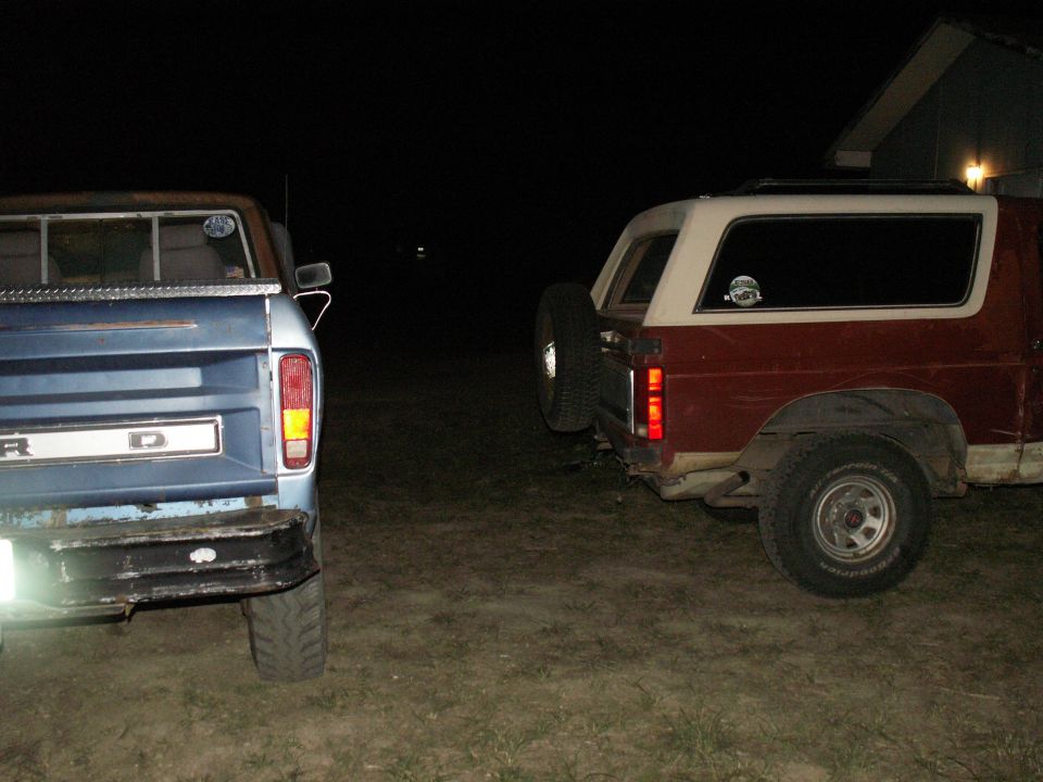 Rear view of a blue Ford pickup truck and a red Ford Bronco parked side-by-side at night.