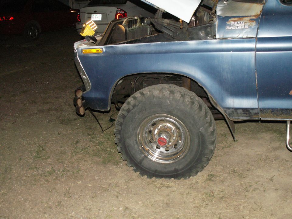 Blue Ford F-250 pickup truck with large off-road tires and custom triple exhaust pipes.