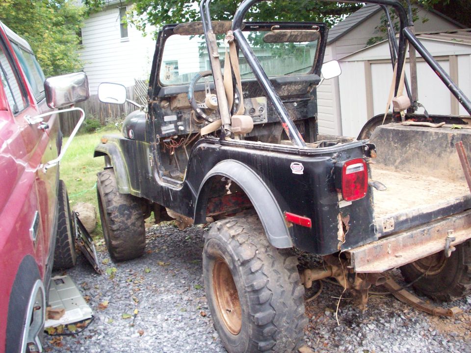 Black Jeep CJ5 with open doors and cargo bed, parked next to a red vehicle.
