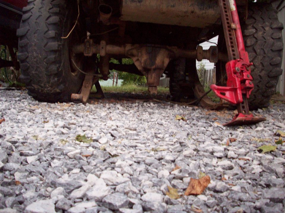 Red Hi-Lift jack under the rear axle of a lifted off-road vehicle with large tires.