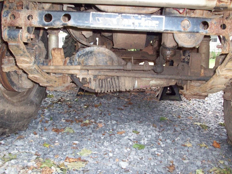 Underside of a rusty vehicle on jack stands, showing suspension and differential.