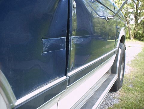 1986 Ford Bronco - Side view of a dark blue 1986 Ford Bronco showing damage to the door panel.