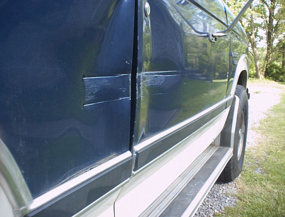 Dark blue 1986 Ford Bronco side door with significant scratches and dents near the handle