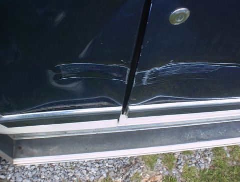 1986 Ford Bronco - Close-up of a dark blue vehicle door showing extensive damage along the seam and lower body panel.