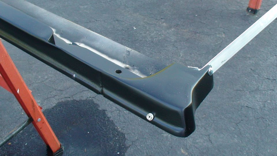 Black-painted rail with aluminum extrusion attached, supported on orange ladders during fabrication