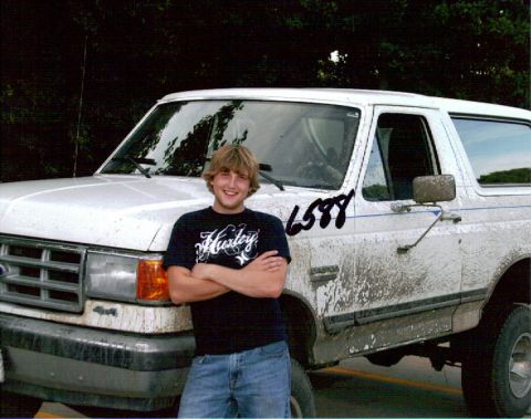 1987 Ford Bronco - A young man with his arms crossed stands in front of a muddy white Ford Bronco. A handwritten number '6588' is visible on the driver's side…