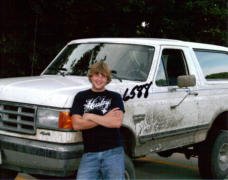 Young man in Hurley shirt poses in front of a muddy white Ford Bronco with '6588' on the door.