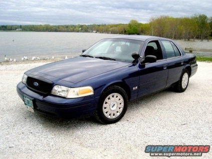 2003 Ford Crown Victoria - A dark blue 2003 Ford Crown Victoria sedan is parked on a gravel lot near a body of water. The car is viewed from a 3/4 front angle, showca…