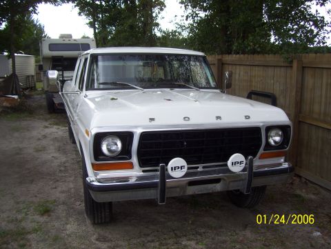 1978 Ford Bronco - A white 1978 Ford Bronco is parked outdoors next to a wooden fence, with a camper trailer visible in the background. The front of the Bronc…