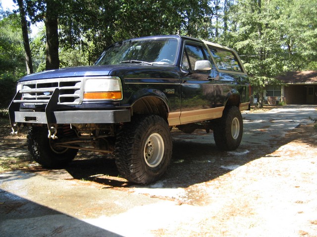 Lifted dark blue 1995 Ford Bronco with custom bumper and off-road tires parked on a driveway.