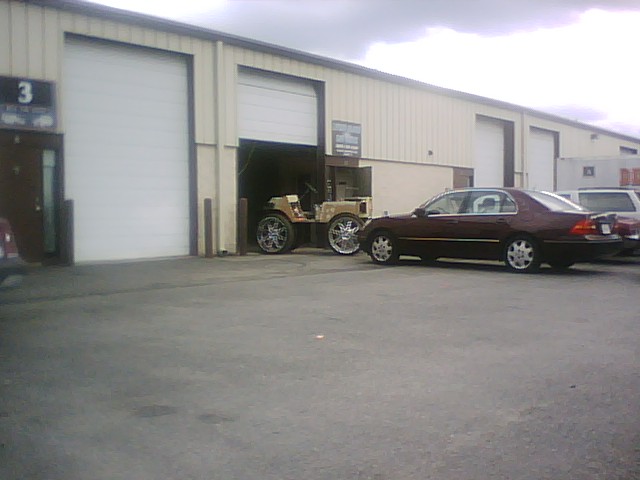 Custom vehicle with large chrome rims in garage bay, maroon sedan parked outside.
