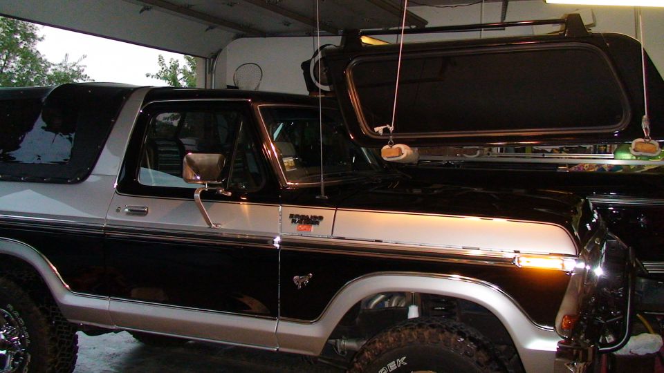 Black and silver Ford Bronco in garage with hardtop lifted off on cables