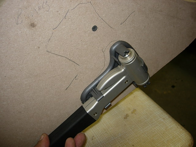 Hand holding a staple gun over a piece of particle board with a drawing.