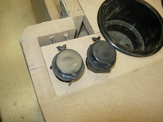 Two black circular caps with flip-up tabs and a black cup holder on cardboard.