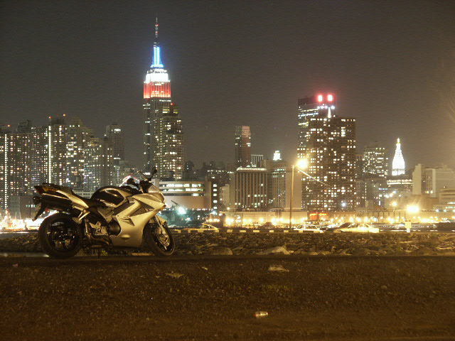 Silver sport motorcycle parked at night with lit Manhattan skyline behind