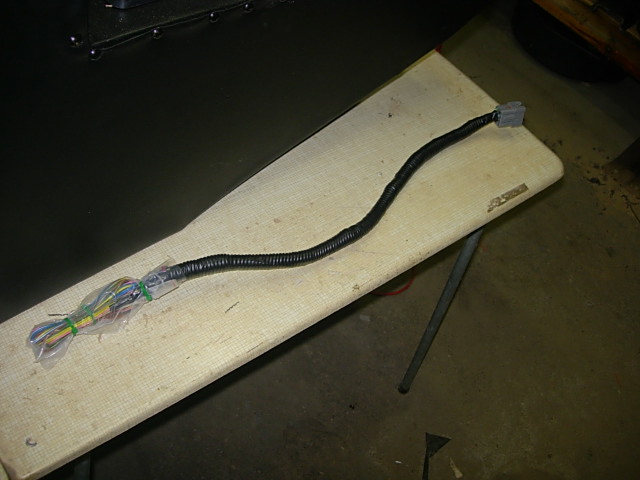 Black wire harness with gray connector and bundled wires on a folding table.