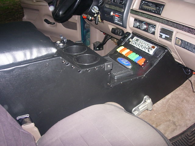 Custom black center console with cup holders, padded armrest, and CB radio in a tan Ford Bronco interior