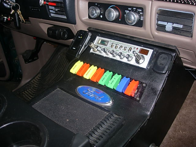 Truck center console with CB radio and ten colored rocker switches beside a Ford oval badge
