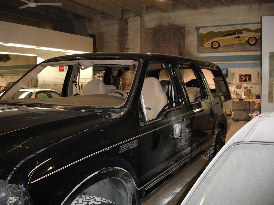 Black Ford Excursion with damaged windshield and side windows removed in a garage.