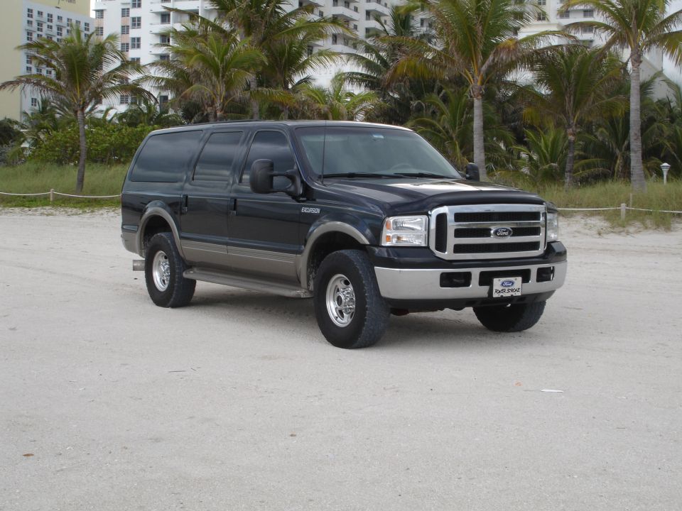 Dark blue Ford Excursion parked on a sandy beach.