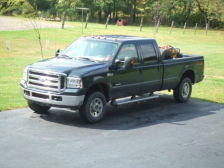 1996 Ford Bronco - A dark green 2005-2007 Ford F-250 Super Duty Lariat SuperCab pickup truck is parked on a paved driveway with a grassy yard and trees in the…