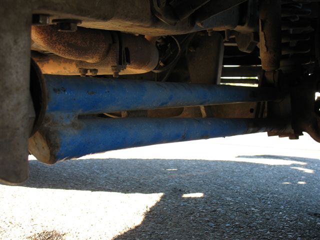 Underside of a vehicle showing blue control arms and rusty exhaust pipe.