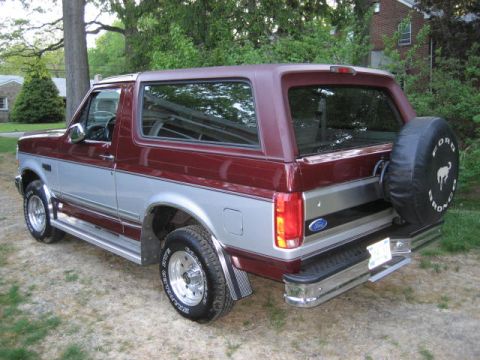 1996 Ford Bronco - Rear three-quarter view of a two-tone red and silver 1996 Ford Bronco with a spare tire cover.