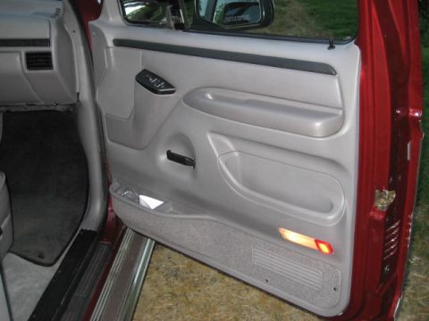 1996 Ford Bronco - The interior door panel features gray plastic trim, a door handle, window controls, and a storage pocket with a red reflector light.