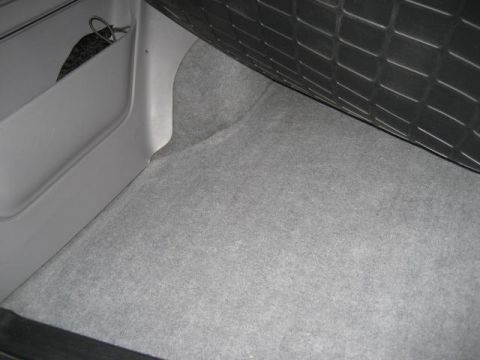 1996 Ford Bronco - The cargo area of a vehicle shows grey carpeting and a side storage compartment.