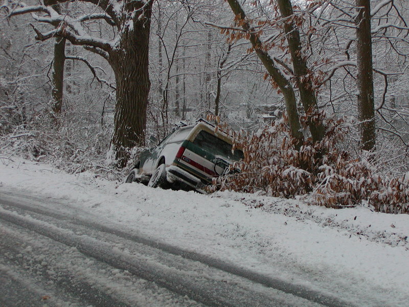 SUV stuck in snow off the side of a road, trees and snow everywhere