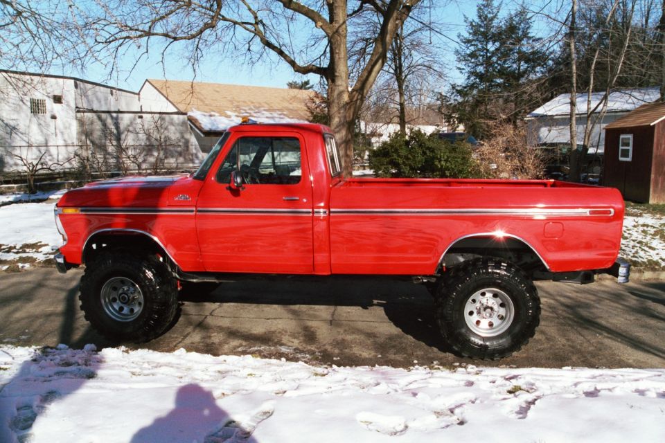 Side view of a red 1979 Ford F-250 pickup truck with large tires, parked on a snowy street