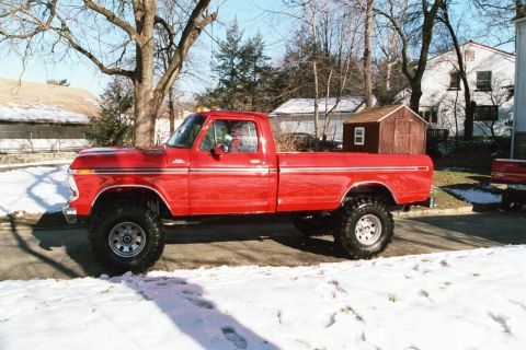 1979 Ford F-250 - A lifted red 1979 Ford F-250 pickup truck sits on a snowy street in front of houses and trees.