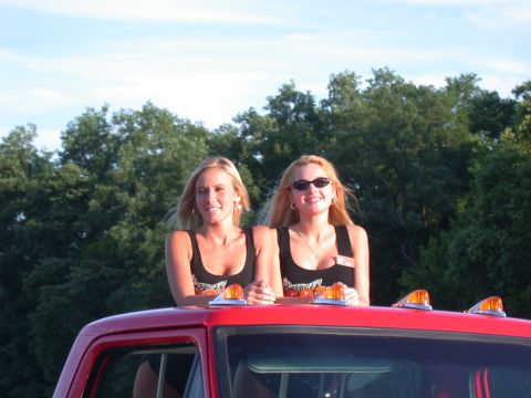 1979 Ford F-250 - Two women pose on the roof of a red truck, with trees and a blue sky in the background.