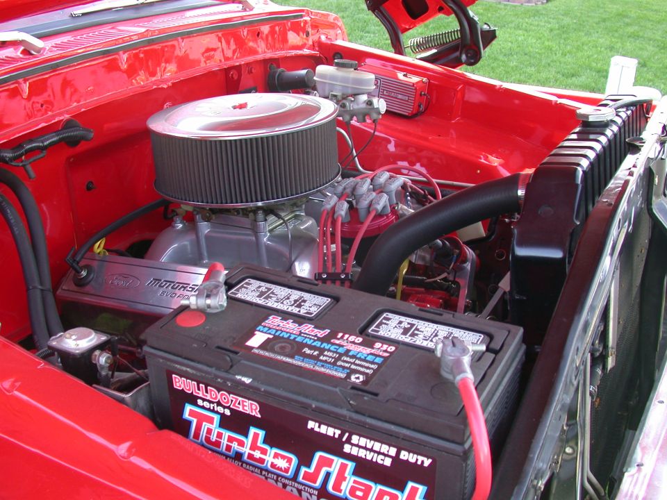 Close-up of a red engine bay with a V8 engine, air filter, and battery