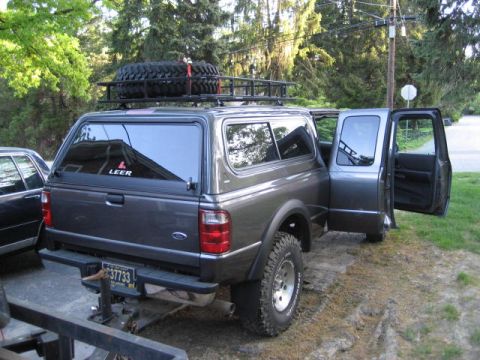 2004 Ford Ranger - A gray Ford Ranger pickup truck is parked with its doors open, a camper shell and a roof rack with a spare tire.