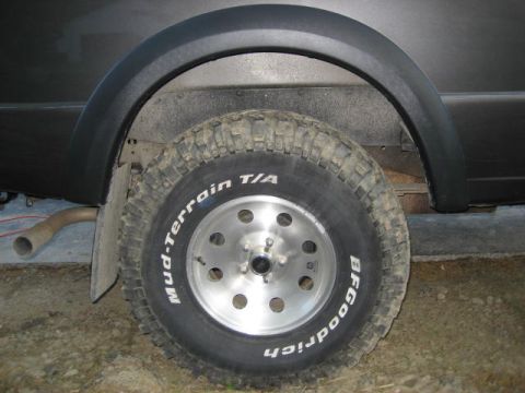 2004 Ford Ranger - A close-up view of a vehicle's rear wheel well and tire, showing off-road tire tread and a silver alloy rim.