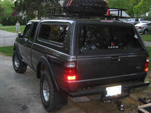 2004 Ford Ranger - A dark gray pickup truck is parked outdoors, equipped with a camper shell and a roof rack carrying a spare tire.