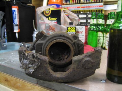1996 Ford Bronco - A heavily rusted brake caliper sits on a workbench next to cleaning supplies and beer bottles.