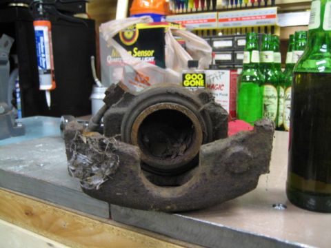 1996 Ford Bronco - A heavily rusted brake caliper sits on a workbench next to cleaning supplies and beer.